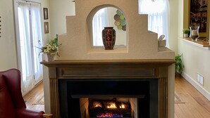 A fireplace with a stone mantle, a red leather chair, and a vase on the mantel.