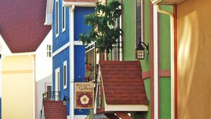 A street with colorful buildings, a green trash bin, and outdoor seating with umbrellas.