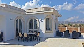 A covered patio with a table and chairs, large arched windows, and a view of the countryside.