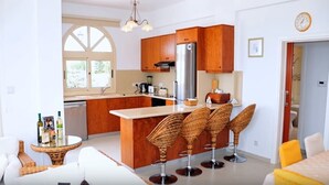 A modern kitchen with wooden cabinets, a stainless steel refrigerator, and a bar area with wicker stools. - Acropolis Sea View Villa - Panoramic Views & Stunning location (Poli Crysochous)