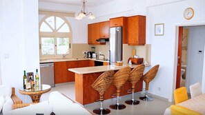 A modern kitchen with wooden cabinets, a stainless steel refrigerator, and a bar area with wicker stools.
