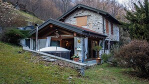 A stone house with a sloped roof, a wooden porch, and a small garden area.