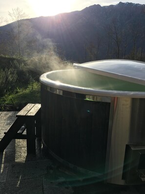 Un jacuzzi con un banco de madera en un entorno natural, con montañas al fondo.