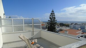 Un balcón con vista al mar, una silla y un ventanal con paneles de vidrio esmerilado.