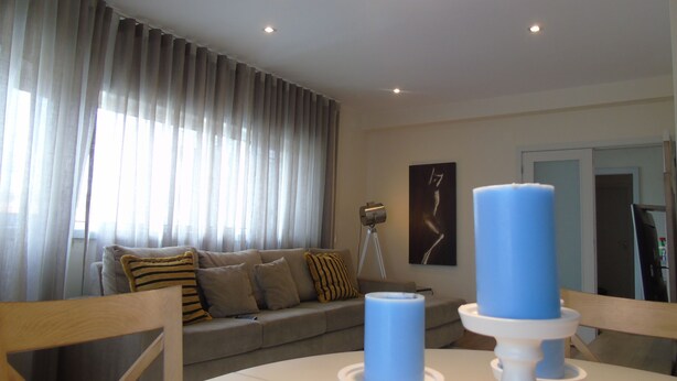 Una sala de estar moderna con un sofá, una mesa de comedor con velas y un amplio ventanal con cortinas.