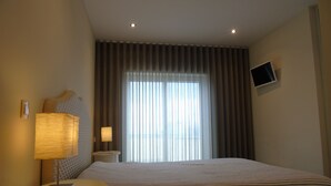 Habitación de hotel con cama, dos lámparas de noche, televisor de pantalla plana en la pared y ventana con cortinas.