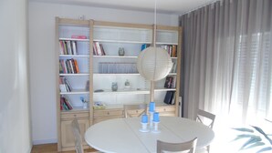 Un comedor con una mesa redonda, sillas y una estantería llena de libros y adornos.