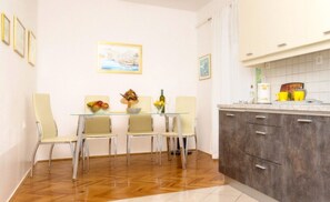 A dining area with a glass table and four chairs, a kitchen with grey cabinets, and a painting on the wall. - Apartment for 4 persons with sea view, WiFi, Parking, BBQ - Adress: Kremenici 26 (Malinska)