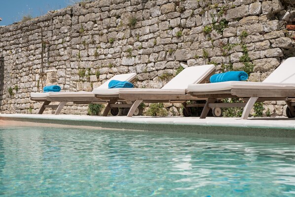 A poolside area with stone walls and lounge chairs.
