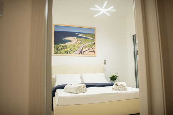 Een opgemaakt bed met opgerolde handdoeken, een lijst met een landschapsafbeelding erboven en een lamp met sterrenvorm.