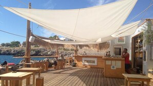 Une terrasse en bois avec des tables et des chaises, un coin bar et une vue sur la mer.