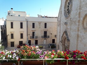 A courtyard with a row of colorful flowers, a building with a balcony, and a church with ornate architecture. - In the heart of Conversano with a splendid view of the Duomo - Il Nido delle Rondini (Conversano)