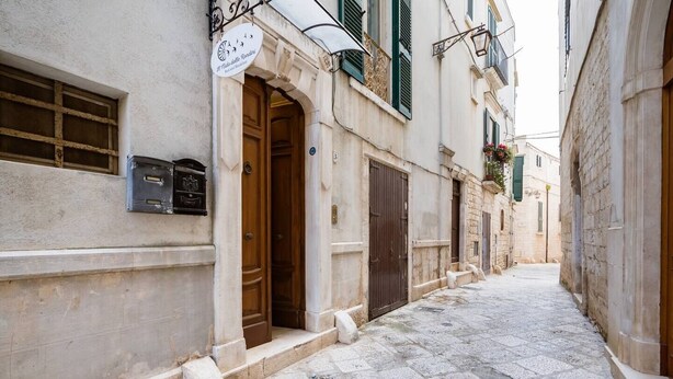 A narrow street with stone buildings, wooden doors, and a sign above a door. - In the heart of Conversano with a splendid view of the Duomo - Il Nido delle Rondini (Conversano)