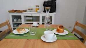 A wooden dining table with a green placemat, two white plates with pastries, a coffee maker, and a glass pitcher on a white cabinet. - Large apartment in the center of Lecce (Lecce)