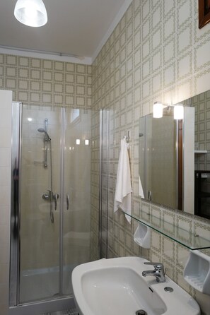 Un baño con ducha envuelta en vidrio, un lavamanos blanco y un espejo con repisa de vidrio.