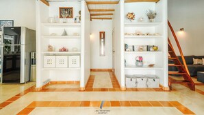 Un vaste espace de vie doté d’un plafond haut, de poutres en bois et d’un couloir central menant à un escalier.