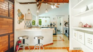 Une cuisine moderne dotée d’un îlot central, de tabourets de bar, d’un ventilateur de plafond et offrant une vue sur la salle à manger adjacente.
