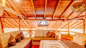 L’intérieur d’un chalet en bois, avec un lit, un canapé, une table de chevet et un ventilateur.