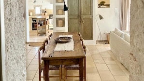 Un comedor con una mesa y sillas de madera, una lámpara colgante y una cocina al fondo.