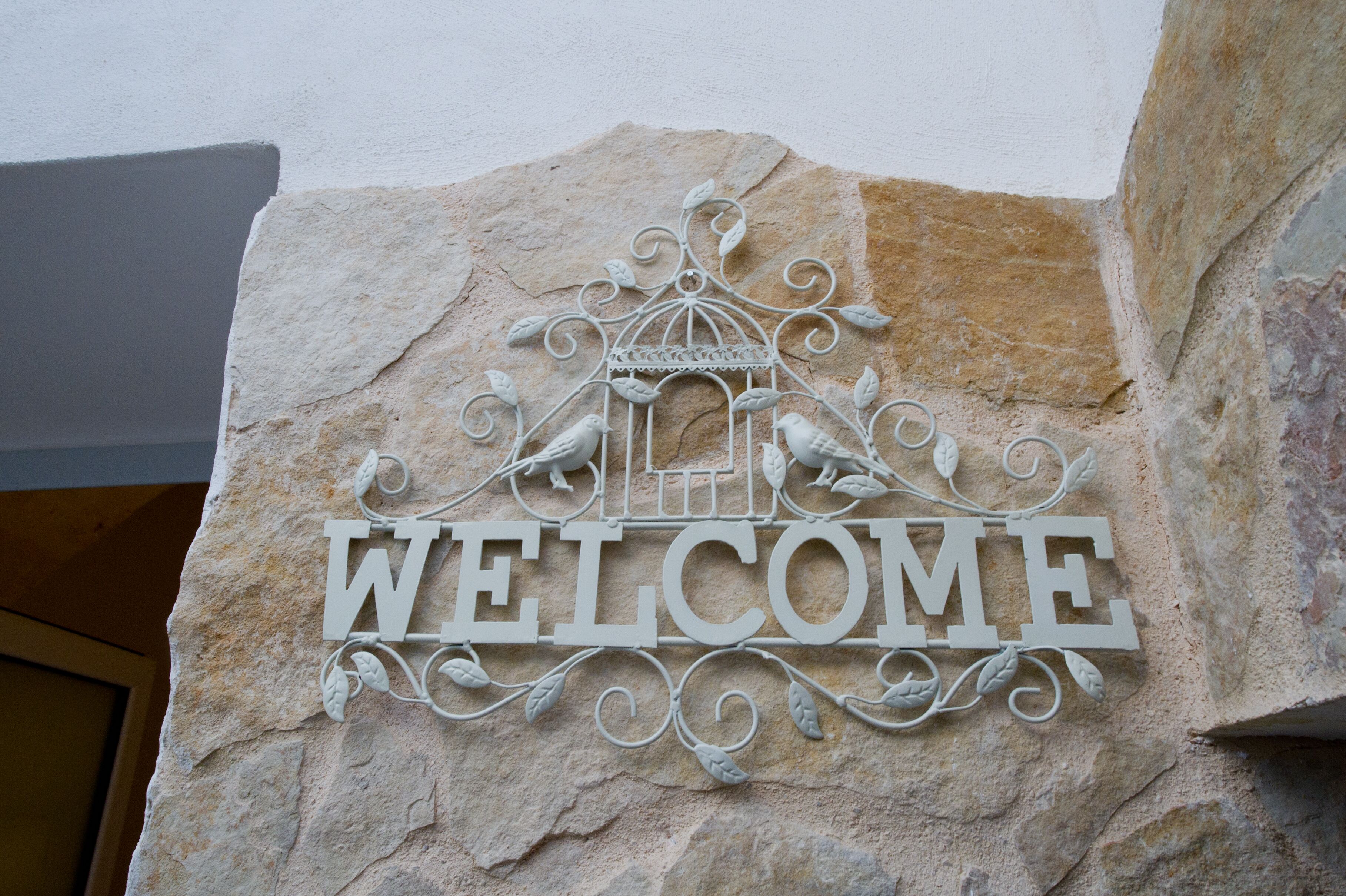 A welcome sign with a birdcage design on a stone wall.