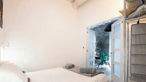 A bedroom with a bed, a small table, and a chair. There is a door leading to a balcony. - BartoloBeachApartment. 100m from La KONTXA Beach (Donostia)