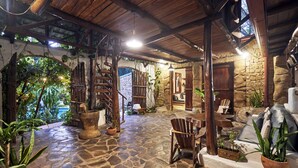 Un patio rústico al aire libre con suelo de piedra, mobiliario de madera y abundante vegetación.