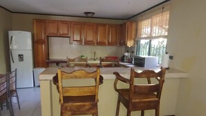 A kitchen with wooden cabinets, a refrigerator, a microwave, and two wooden chairs.