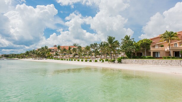 Un hotel frente a la playa con arena dorada, palmeras y agua turquesa cristalina.