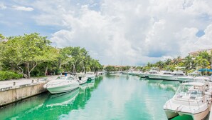 Un puerto deportivo con varias embarcaciones amarradas a lo largo de una vía fluvial tranquila, rodeado de exuberante vegetación y un cielo despejado.
