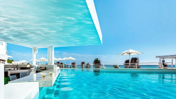 A pool area with clear blue water, white umbrellas, and a view of the ocean. - The Most Amazing Views! Beachfront Penthouse 3BR3/Bth (Cancun)