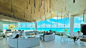 A modern lobby with a large seating area, a reception desk, and a view of the ocean. - The Most Amazing Views! Beachfront Penthouse 3BR3/Bth (Cancun)