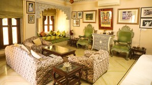 A traditional room with a sofa set, a green armchair, a small table, and a decorative mirror. - Venus Heritage in the family  (Udaipur)