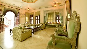 A spacious living room with a high ceiling, ornate ceiling design, and a large mirror. - Venus Heritage in the family  (Udaipur)