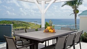 A covered patio with a table and chairs, overlooking a coastal view with a tropical landscape and the ocean. - Les Alizés, magnificent villa with breathtaking view (Oyster pond)