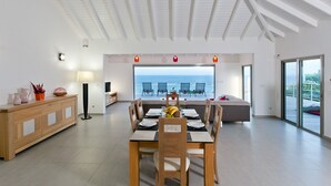 A spacious dining area with a view of the sea, a wooden dining table, and a seating arrangement. - Les Alizés, magnificent villa with breathtaking view (Oyster pond)