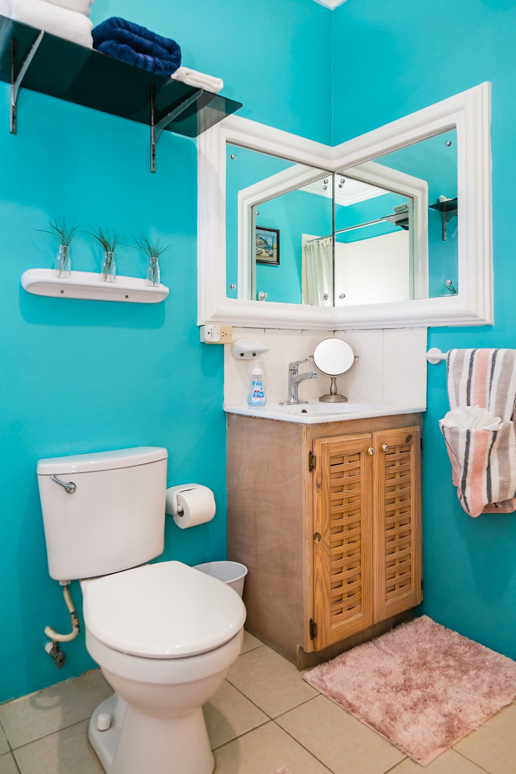 A bathroom with a white toilet, a sink with a mirror, a wooden cabinet, and a blue wall.