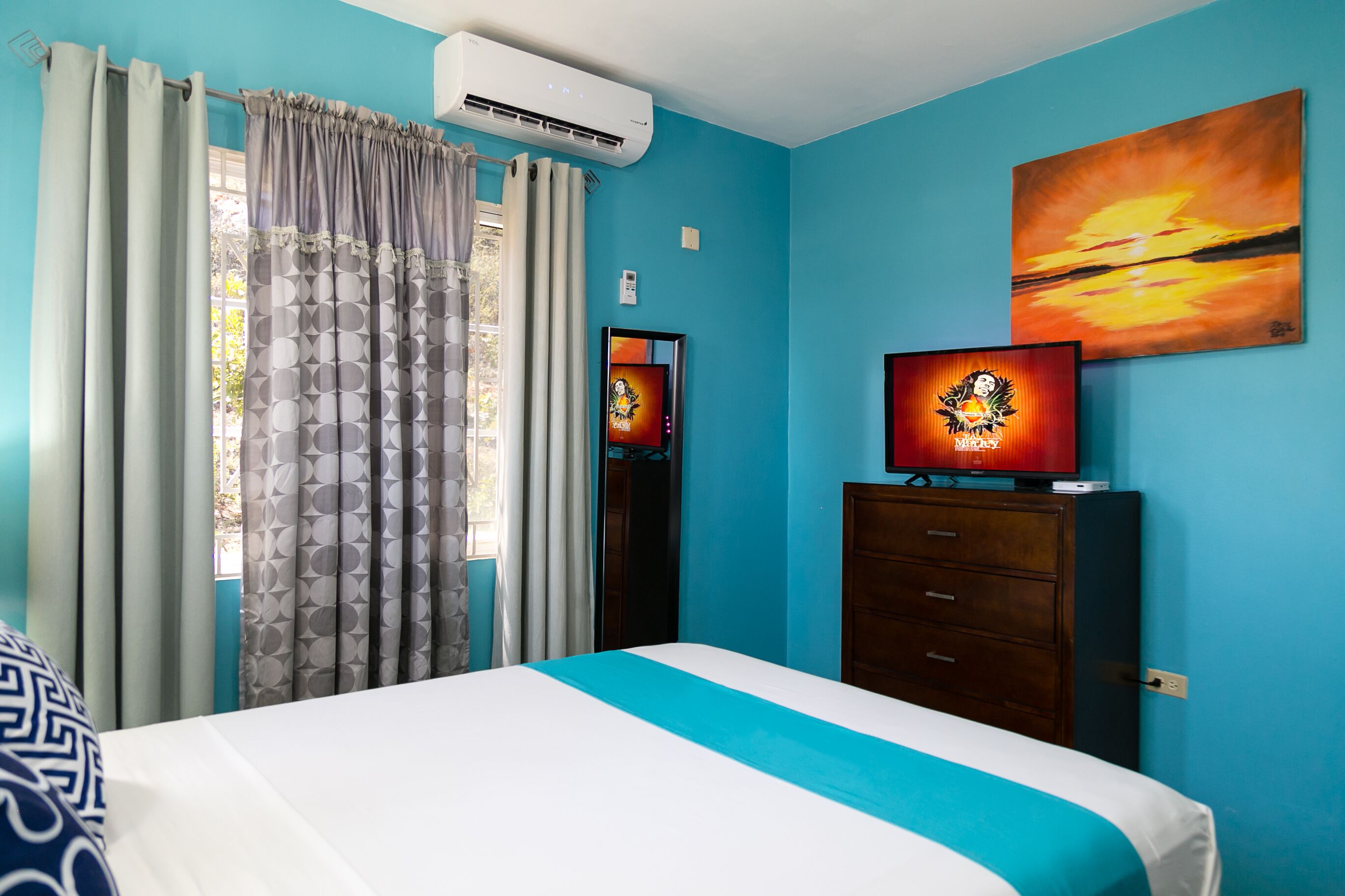 A bedroom with a bed, a TV, a dresser, and a painting on the wall.