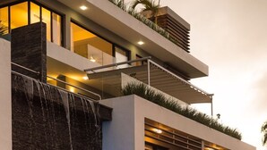 A modern multi-story building with a waterfall feature, outdoor seating, and a balcony with plants. - 5 star BEACH VIEW DUPLEX W/ PRIVATE POOL, JACUZZI (Las Terrenas)