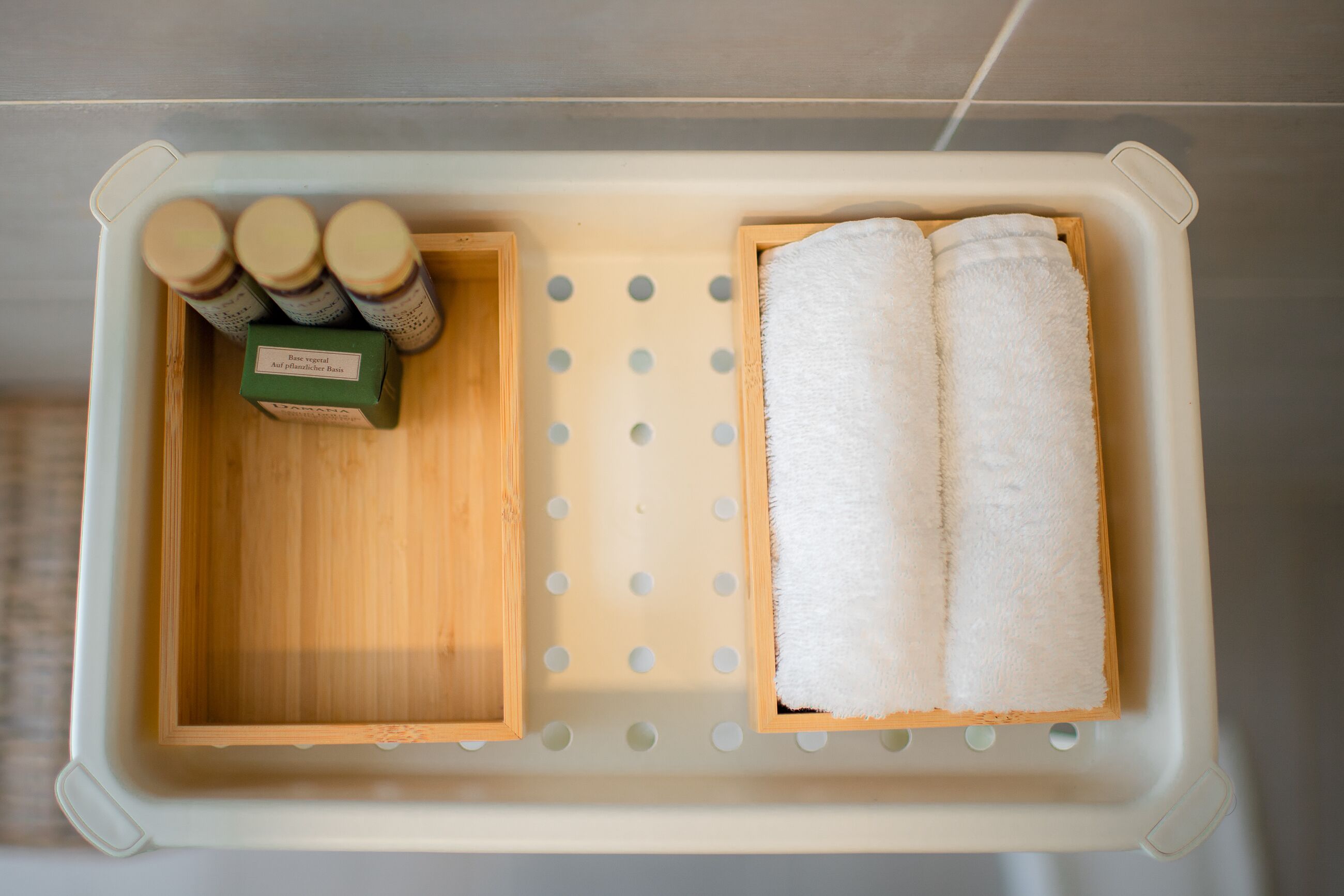 A bathroom with a white sink, a wooden tray with a green soap dish, and two towels.