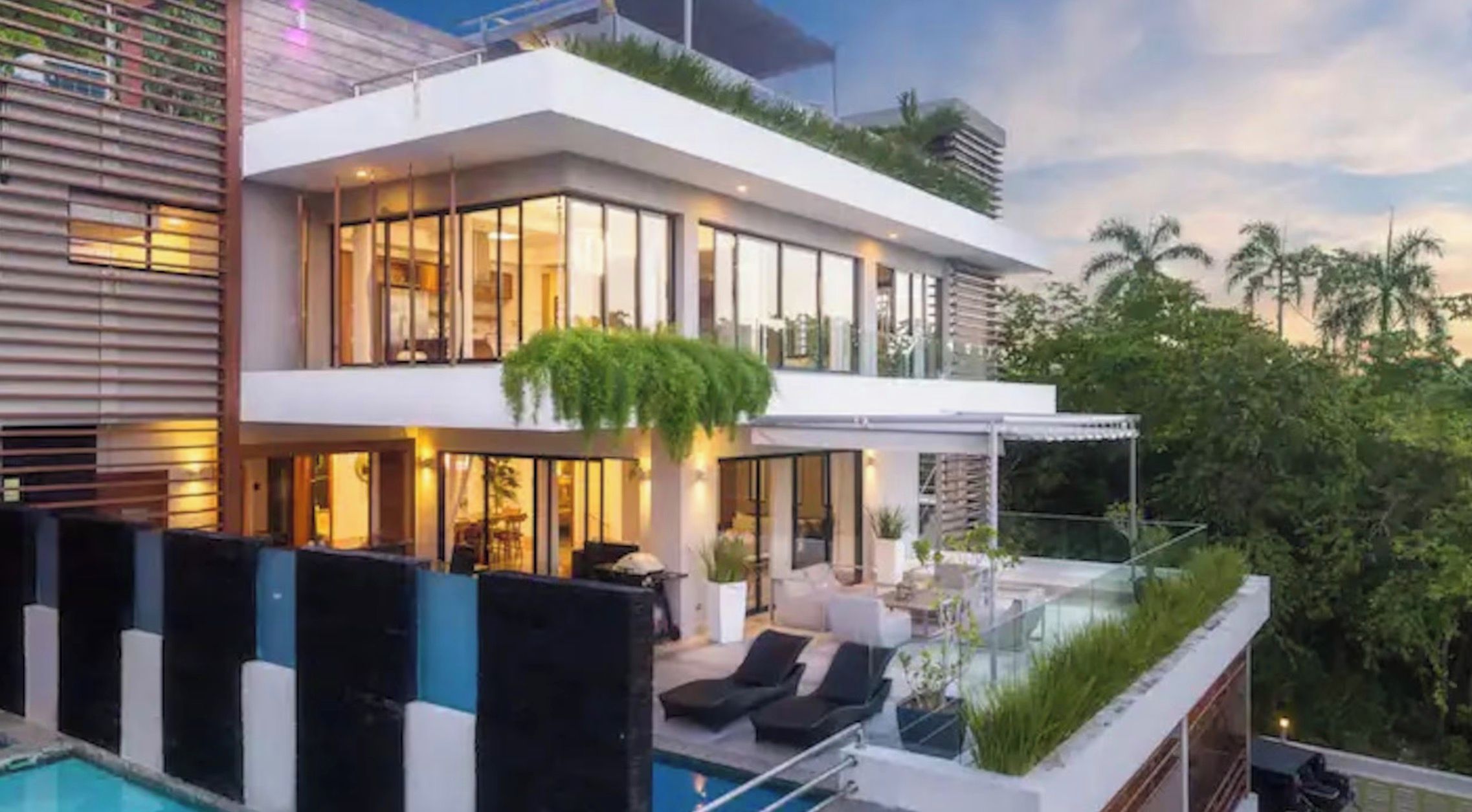A modern two-story building with a rooftop pool area, large windows, and outdoor seating.