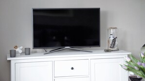 A flat-screen TV on a white cabinet with a glass vase containing a decorative item and a small card. - ELBQUARTIER | Charming apartment with elevator right in the center (Wedel)
