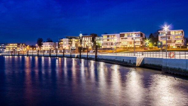 A waterfront hotel with modern architecture, a reflective pool, and well-lit balconies. - ELBQUARTIER | Charming apartment with elevator right in the center (Wedel)