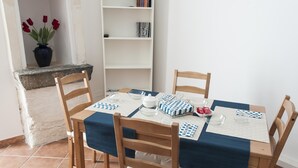 Un coin repas avec une table dressée pour quatre personnes, entourée de chaises en bois, d’une bibliothèque et d’un vase rempli de fleurs rouges.