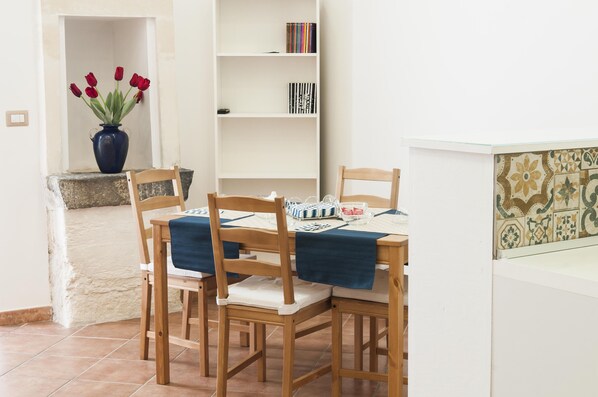 A dining area with a wooden table and chairs, a vase of red tulips, a bookshelf, and a tiled backsplash.