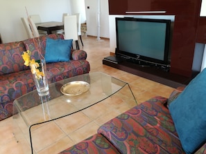 Un salon avec un canapé, une table basse en verre, un téléviseur et un mur décoré d’un motif.