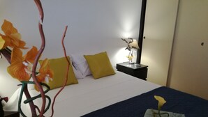 Une chambre d’hôtel avec un lit, des oreillers, une table de chevet avec une lampe et une plante décorative.
