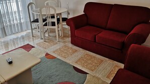 Ein Wohnzimmer mit einem roten Sofa, einem kleinen Tisch und einem Essbereich mit Stühlen.