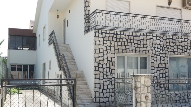 Ein modernes, zweistöckiges Haus mit Natursteinfassade, einem Metalltor und einer Treppe, die zum oberen Stockwerk führt.