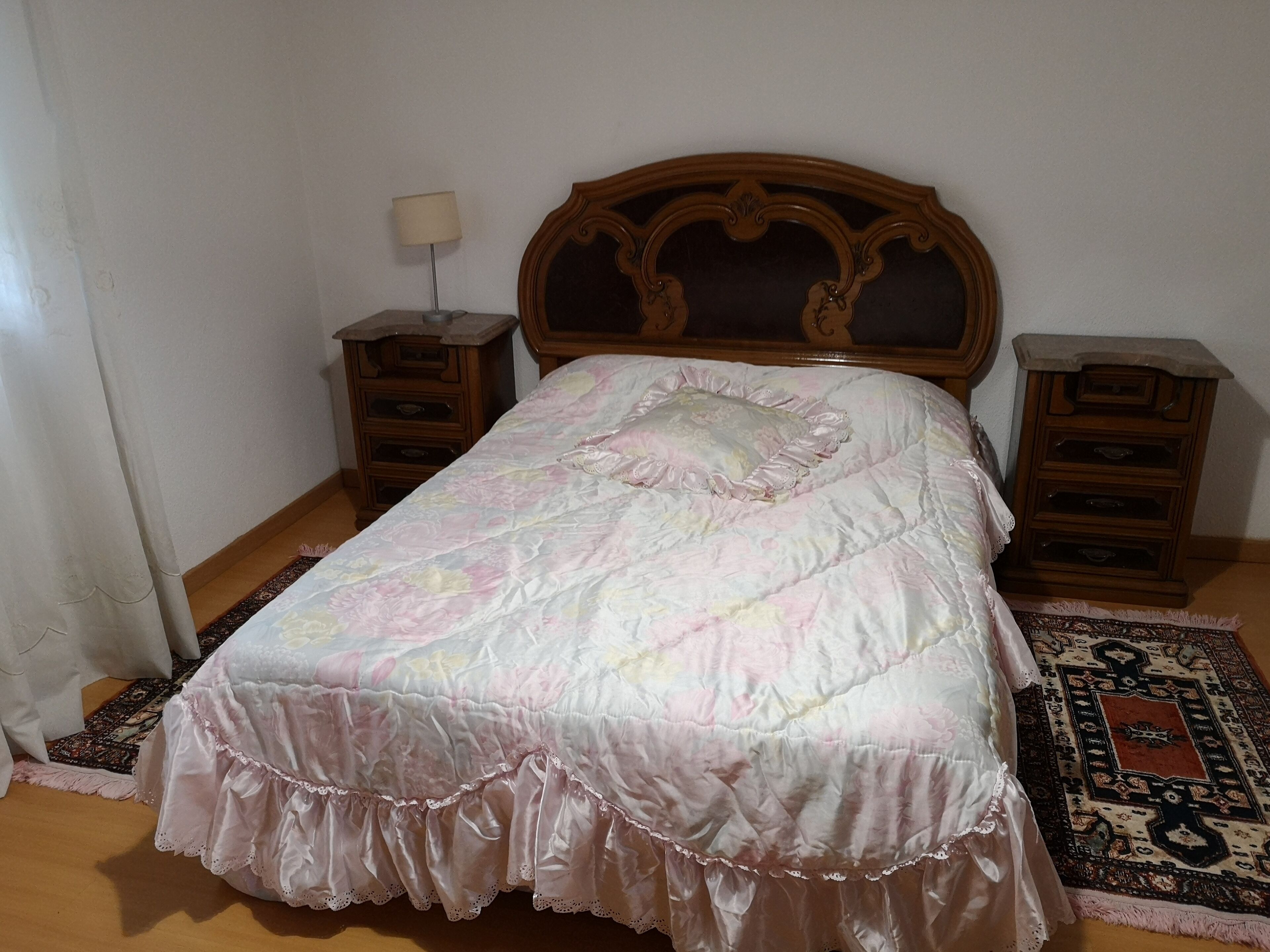 A bedroom with a wooden headboard, a floral bedspread, two nightstands, and a patterned rug.