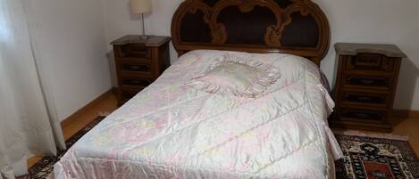 A bedroom with a wooden headboard, a floral bedspread, two nightstands, and a patterned rug.